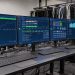 Espace professionnel bleu montrant plusieurs écrans de supervision cybersécurité et des baies de serveurs dans une agence web.
